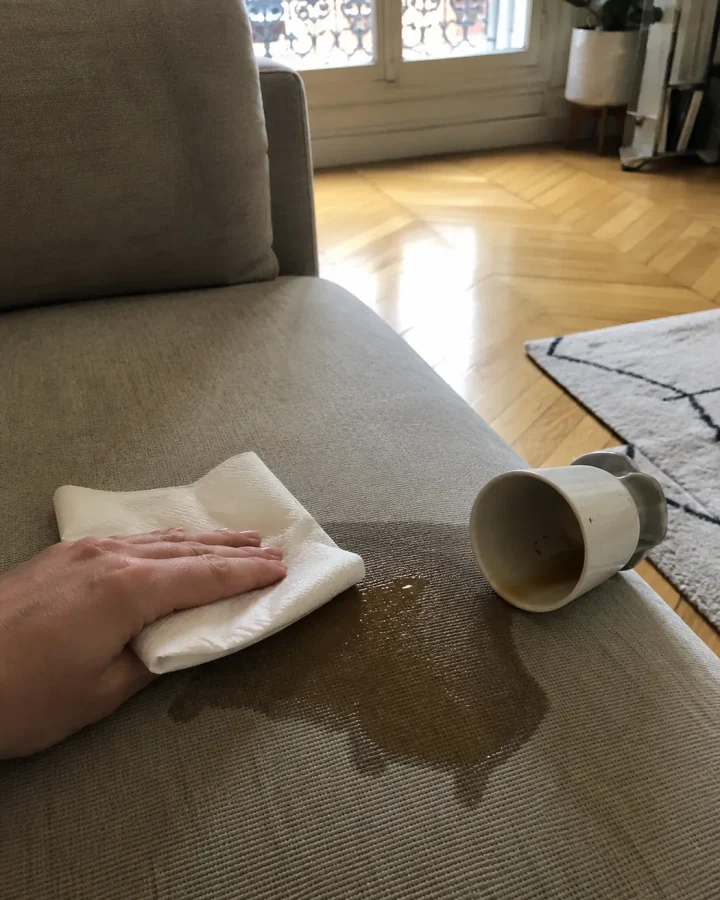 Main tamponnant avec du papier absorbant une tache de café fraîche sur l'assise d'un canapé en tissu beige