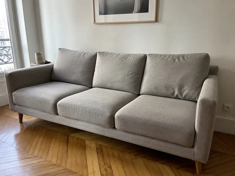 Canapé trois places en tissu gris clair dans un salon parisien au parquet en point de Hongrie